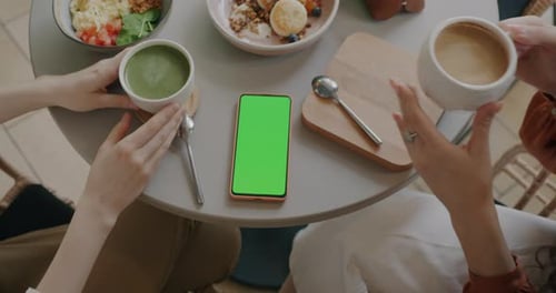 Top View of Smart Phone with Green Screen Chroma Key and Female Hands with Coffee Cups at Table in