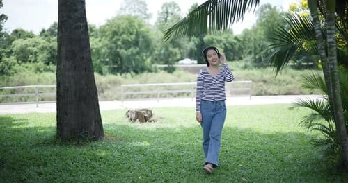 Happy Asian woman wearing wireless headphones enjoying listening to music in fresh air in a park
