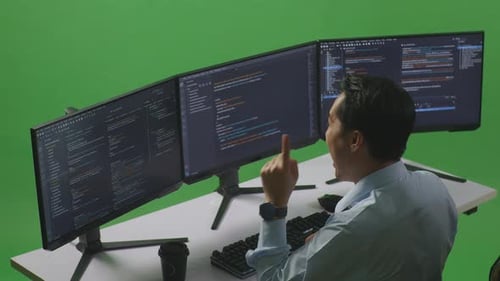 Side View Of Asian Man Thinking While Write Code With Multiple Computer Screens In Green Screen