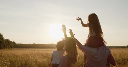 Young Happy Family of Four Spend Time in a Golden Field at Sunset