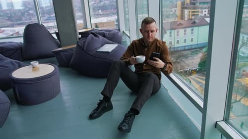 Man Uses Phone While Drinking Coffee in Office