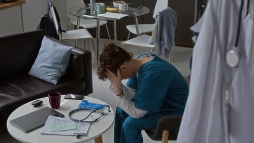 Weary Healthcare Worker Sitting at Home in Scrubs