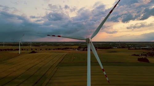 Wind Power Turbine Rotating Rotor Blades with Agricultural Fields on Background During Sunset with