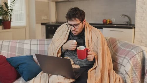 Man Under Blanket With Mug Using Laptop