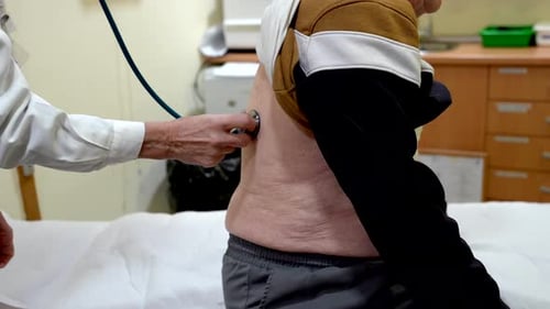 Doctor Examining Senior Man's Lungs with Stethoscope in Nursing Home