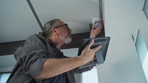 Man Adjusting Security Camera with Tablet in Office
