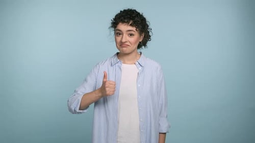 Positive Young Curly Woman Showing Thumb Up Gazes Happy at Camera and Enjoying Posing on Blue