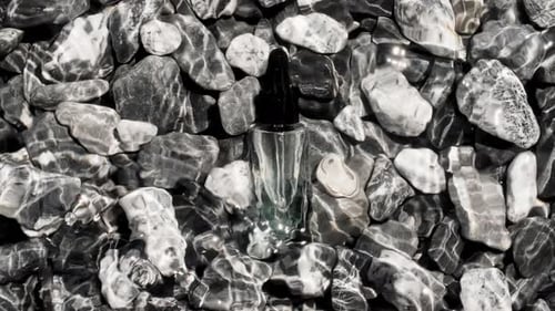 Glass Cosmetic Bottle with Pipette Lies on Pebbles From the Beach Sea Waves On Pebbles Water Surface
