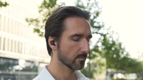 A Handsome Caucasian Man Listens to Music with Earphones on in an Urban Area Closeup