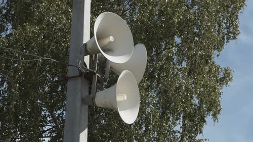 A set of white loudspeakers attached to a pole.