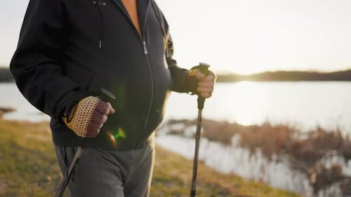 Active Handsome Elderly Man with Nordic Walking Sticks Walks Forward Through Along the Lake at