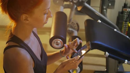 Beautiful sporty surfing internet and social by mobile phone after training at gym close-up