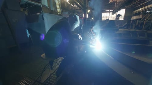 Ein Schweißer, der sein Handwerk in einer industriellen Umgebung mit hellem Schweißbogen, sichtbarer Schaft, ausübt