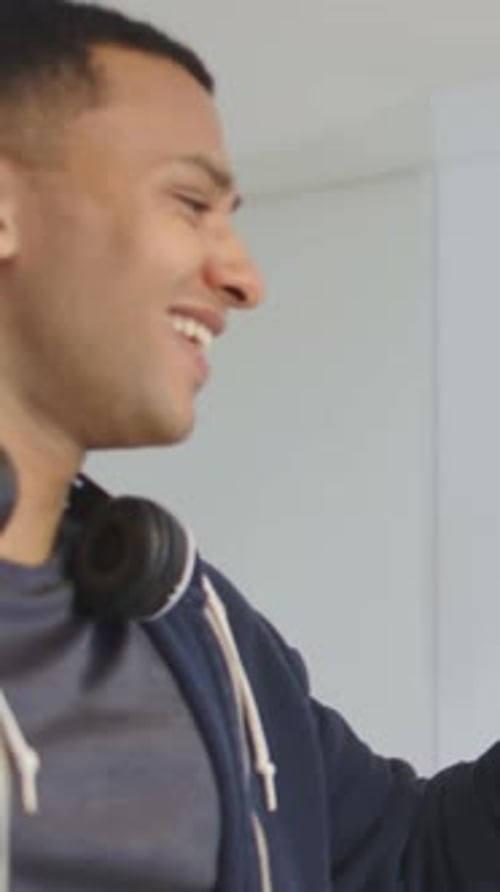 Vertical video: Noticing glass, man in hoodie headset reaching, sipping drink in kitchen to refresh