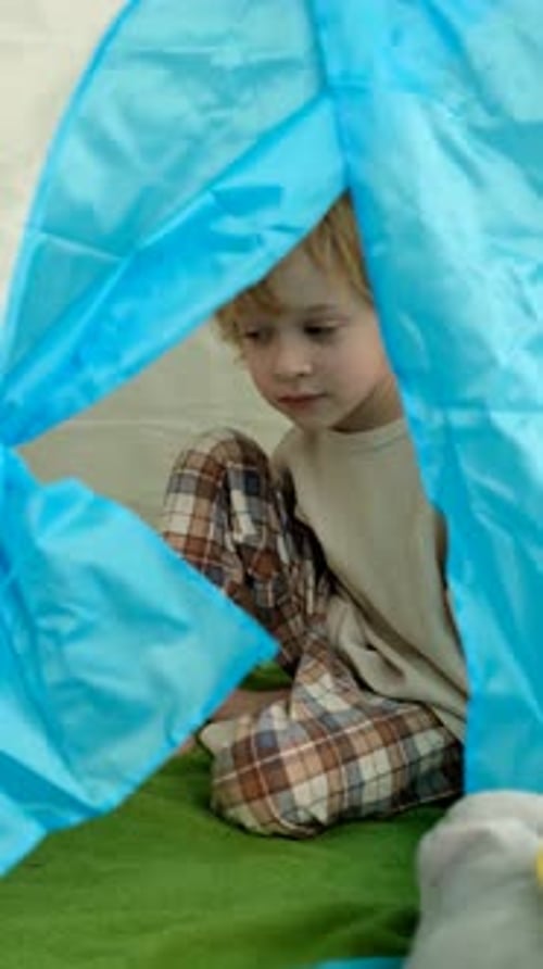 Portrait of a boy laying down a green blanket in a play tent