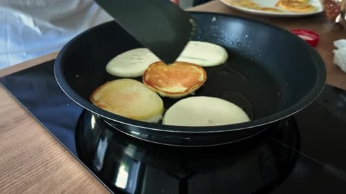 Close-up of a person flipping fluffy pancakes in a non-stick frying pan on an electric stovetop,