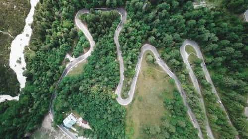 Bird's eye drone shot with a sideways movement of a winding road inside a forest and cars passing by