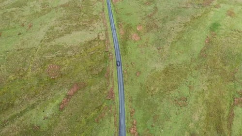 Aerial view following a black car traveling along a country road, in the English Lake District.