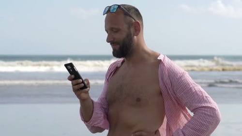 Happy Man Talking on Cellphone Standing on Beach 30s