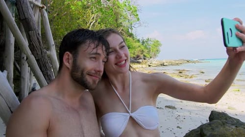 Carefree young couple capturing memories on a Thailand beach with a smartphone