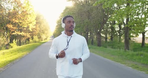 Portrait of Young Handsome Afro Male Athlete Jogging Outdoors Alone on Street Listening to Music in