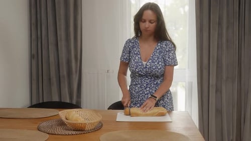 Woman Slicing Baguette at Kitchen Table