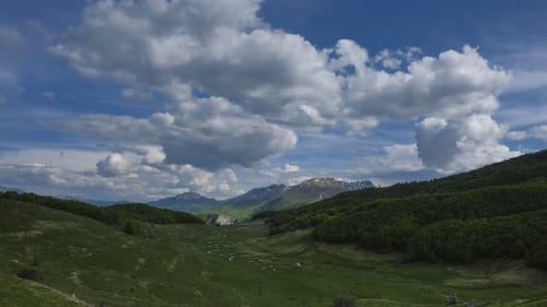 Time lapse of rolling hills and snow capped mountains under a vast sky filled with fluffy clouds