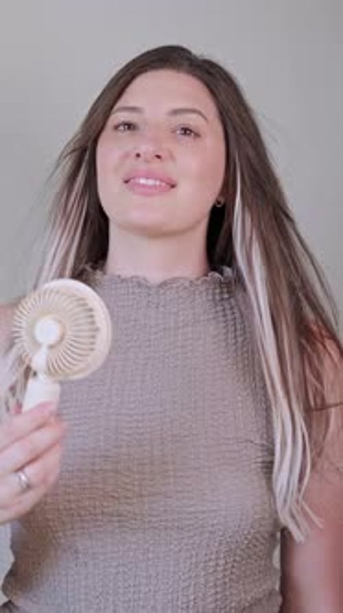 Woman Enjoying Breeze From Handheld Fan Indoors