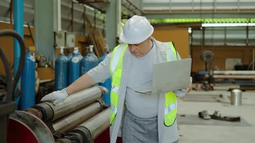 senior male engineer using laptop while inspecting heavy machinery and argon gas cylinders