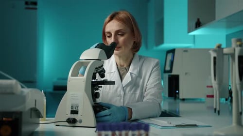 Woman Analyzing Sample Through Microscope in Laboratory