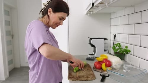 Woman Chopping Cucumber on Cutting Board in Kitchen