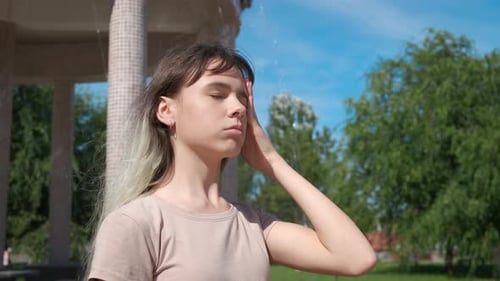 Young Woman Cooling Off in Park Fountain Spray