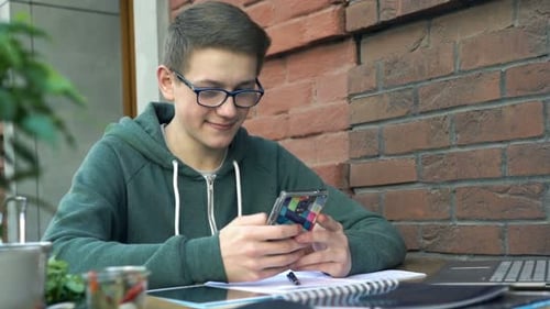 Young Teenager Surfing Internet on Smartphone While Studying in Cafe in City Adolescent