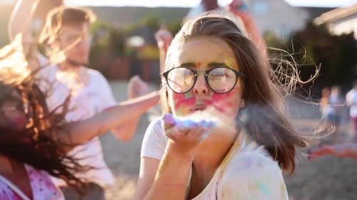 Pretty Woman in Glasses Blows Colored Powder Around at Holi Festival on Beach in Slow Motion Pretty