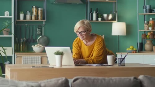 A Woman Freelancer Works at a Computer at Home Looks Through Work Files