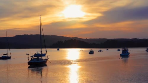 Stand up paddle boarder floating past anchored boats during sunset, lake Whakatane