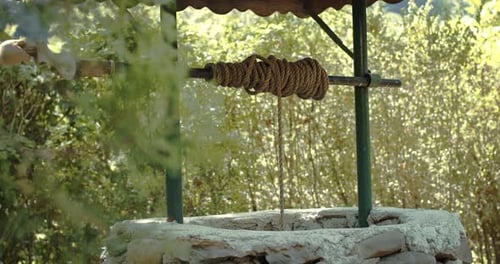 Person Draining Water from Old Vintage Well with Iron Bucket by Twisting Hand in slowmo