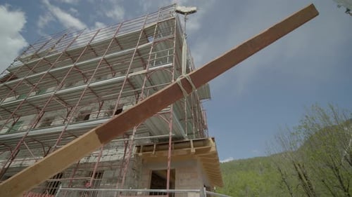 Plano circular de una grúa de gran altura que sostiene un tablón de madera en un edificio en construcción