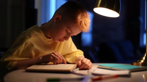 Side View of Focused Cute Little Student Boy Reading Paper Book Following Lines with Finger Along