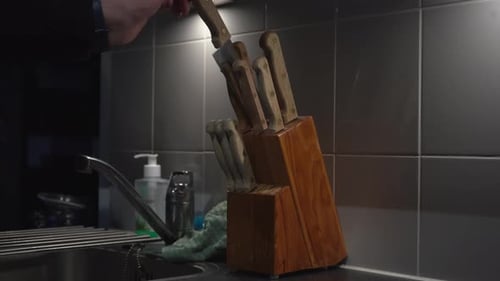 Caucasian hand in tiled kitchen pulls knife from wooden knife block