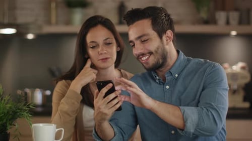 Smiling Couple Using Mobile Phone Together at Home