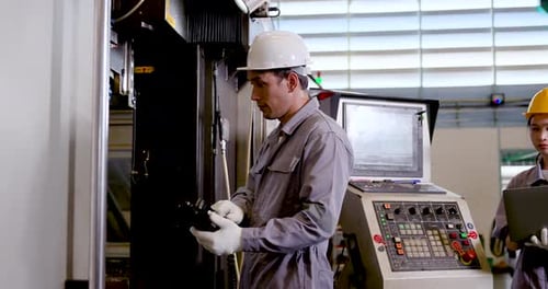 Asian man engineer examines CNC machine area while Asian woman technician reads laptop data,