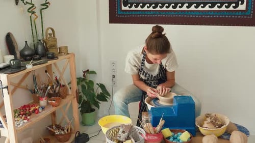 Une potière vêtue d'un jean et d'un tablier travaille sur un tour de potier et fabrique un pot en céramique en argile