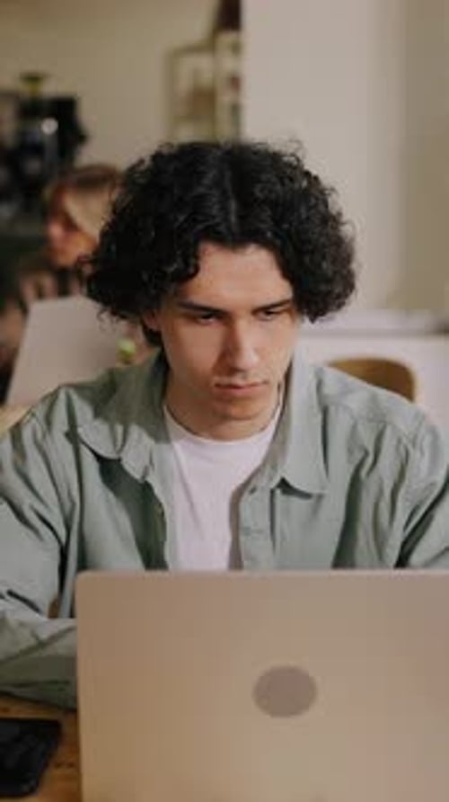 Focused Young Man Working Intently on Laptop Computer in Shared Coworking Space with Casual