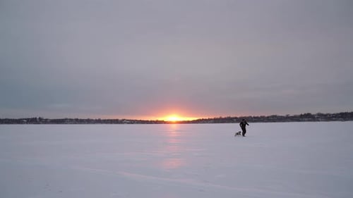 Man with Dog on Frozen Lake at Sunset