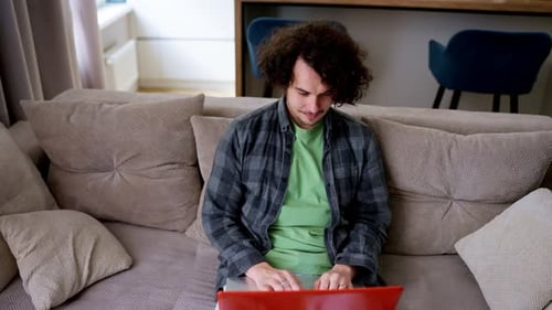 Young Adult Typing on Laptop on Sofa Indoors