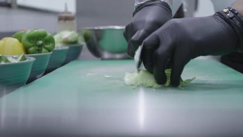 Chef chopping a cabbage using a knife with black gloves on a green cutting board.