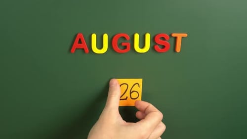 Hand sticking a sticker 26 August calendar day on school board. 26 date of august. Twenty sixth