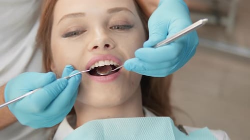 Eine Frau, die sich in einer Klinik von einem professionellen Zahnarzt mit blauen Handschuhen einer zahnärztlichen Untersuchung unterzieht