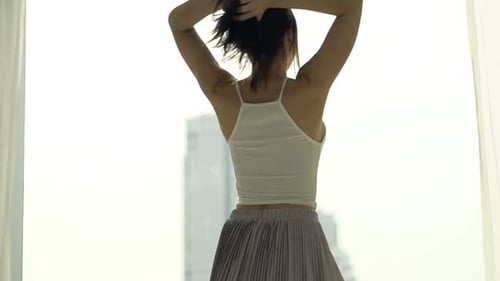 Happy woman dances by window in city apartment